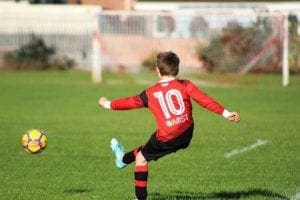 little boy kicking a football with a iMist sponsored shirt on